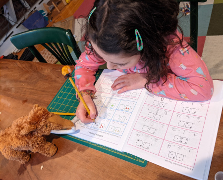 A girl doing math problems from Math Mammoth grade 1 with Mathy the mammoth mascot nearby