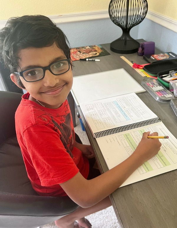 Happily working on Math Mammoth Grade 5 boy sitting at desk with math work, smiling